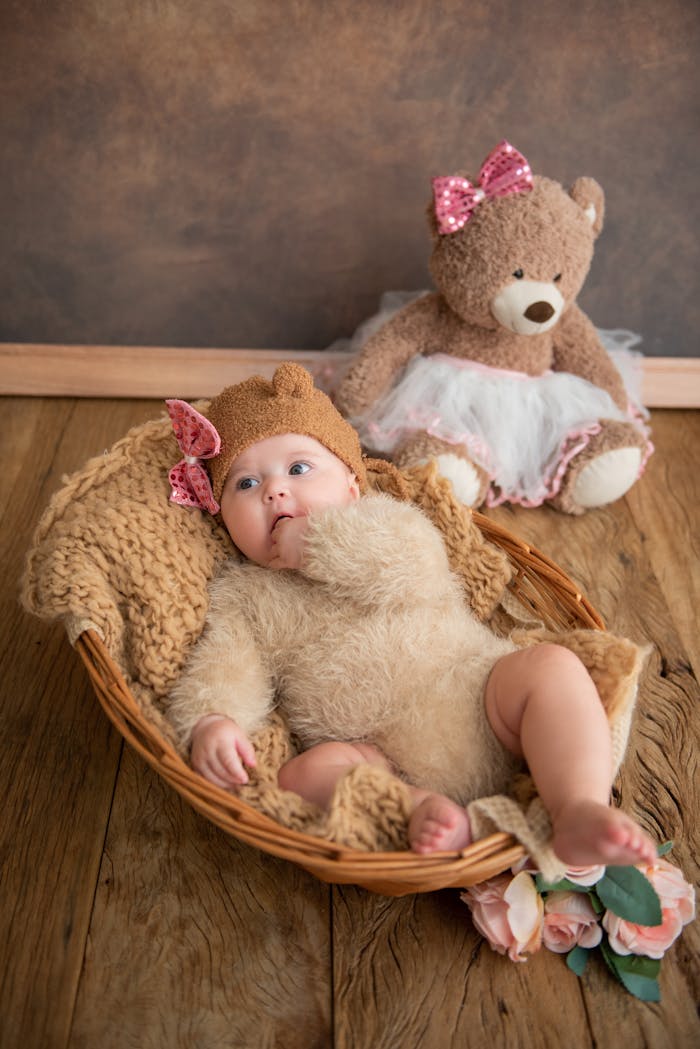 Cute baby dressed in a bear outfit lying in a basket with a plush teddy bear nearby.