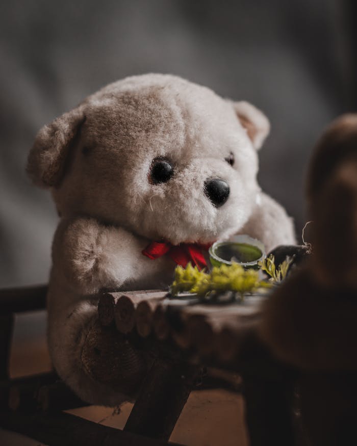 Charming close-up of a teddy bear with a red bow seated at a miniature table. Perfect for childrens themes.