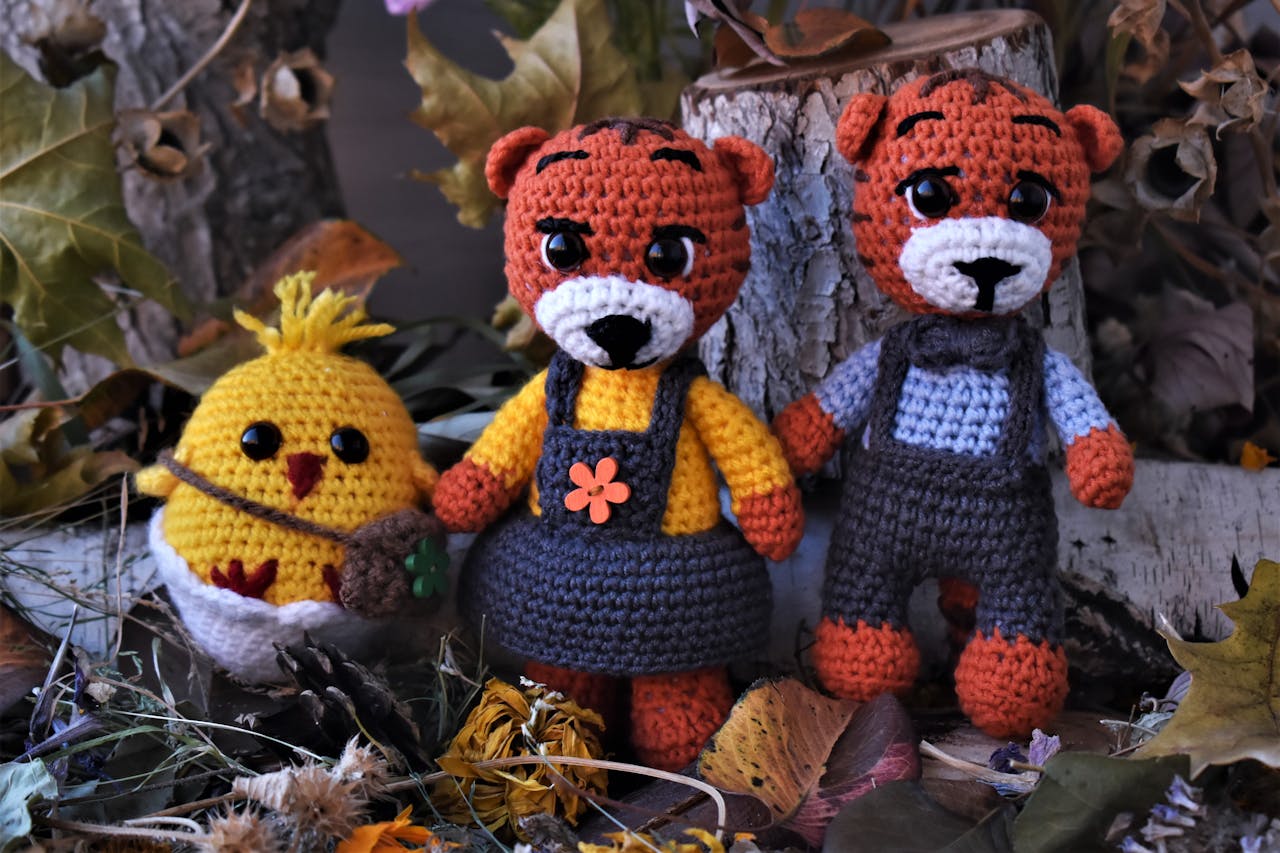 Charming handmade crochet toys pose amidst fallen leaves and tree logs in a cozy autumn scene.